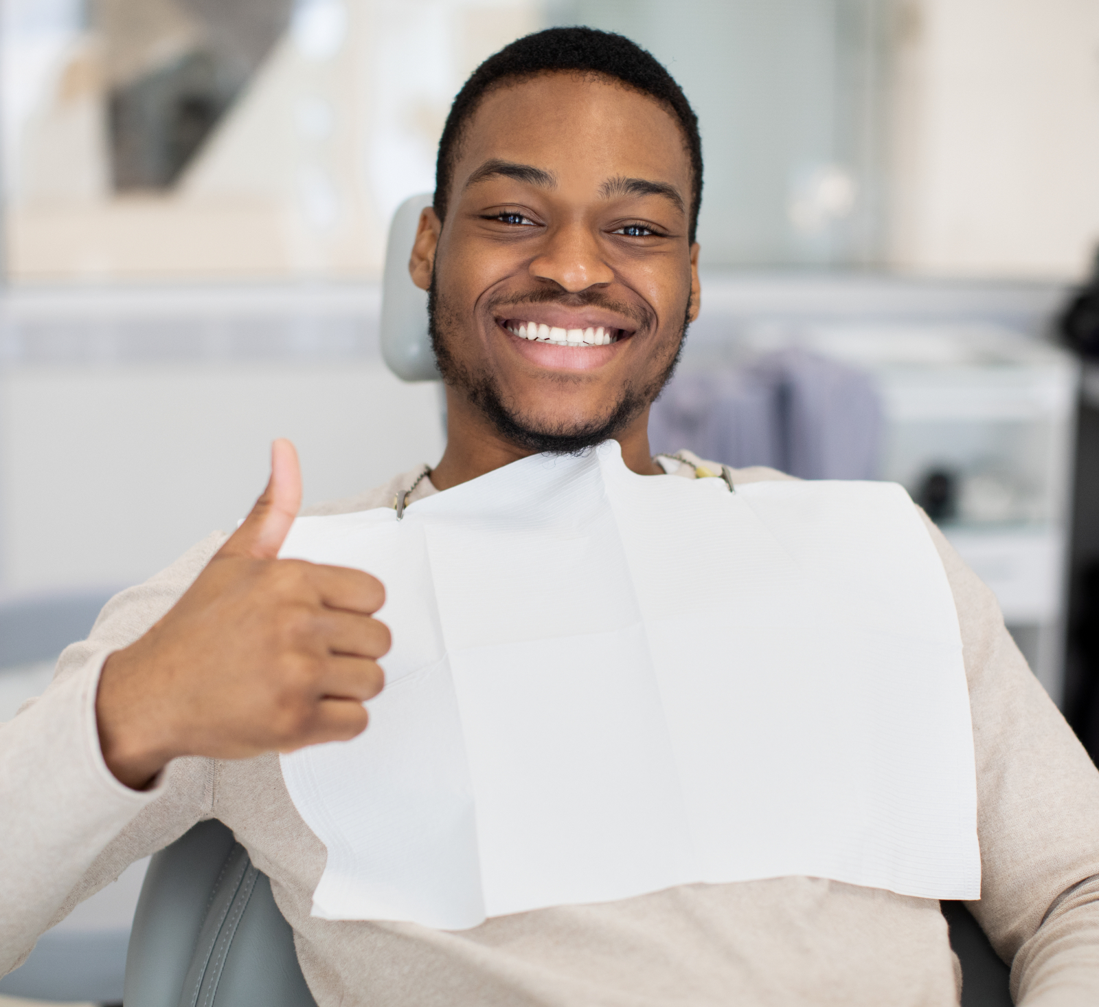 Happy young black man sitting in dentist chair and showing thumb up